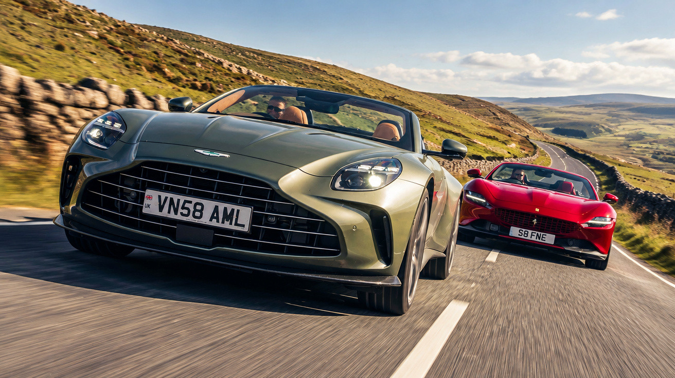 Zwei Sportwagen, ein grüner Aston Martin und ein roter Ferrari, fahren auf einer Landstraße bei sonnigem Wetter.